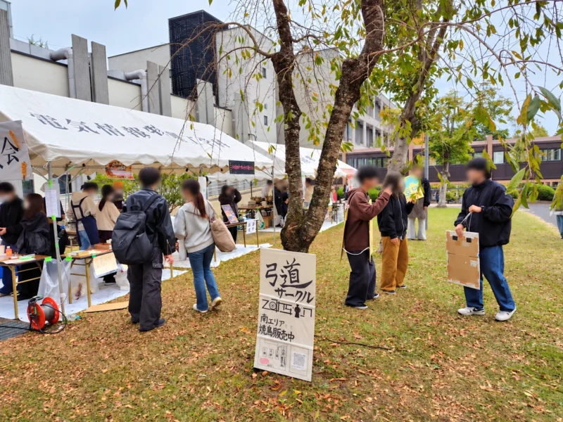 東北大学祭で弓道サークルの看板が掲げられた模擬店と周辺の来場者