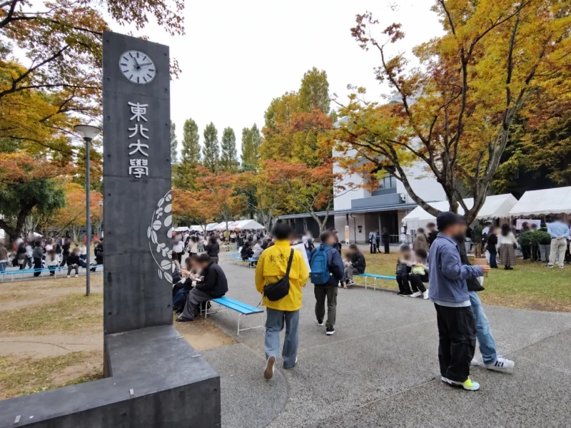 秋の紅葉に囲まれた東北大学の時計塔と大学祭の模擬店や来場者